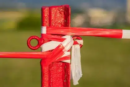 Stewardzi i anonimowi kibice przy barierce stadionu, fragment murawy i buty piłkarskie
